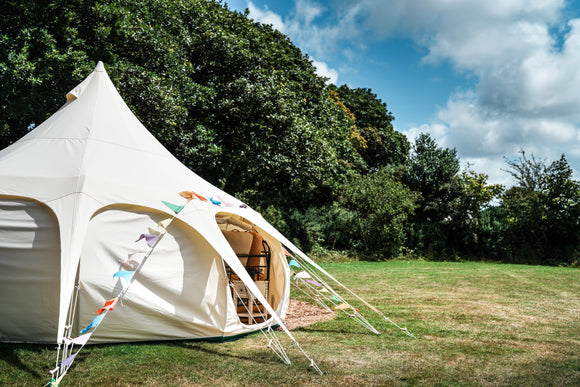Picture of a Lotus Belle Tent pitched in a field. A luxury, canvas bell tent, but with lots of standing room. Perfect for glamping, events & parties